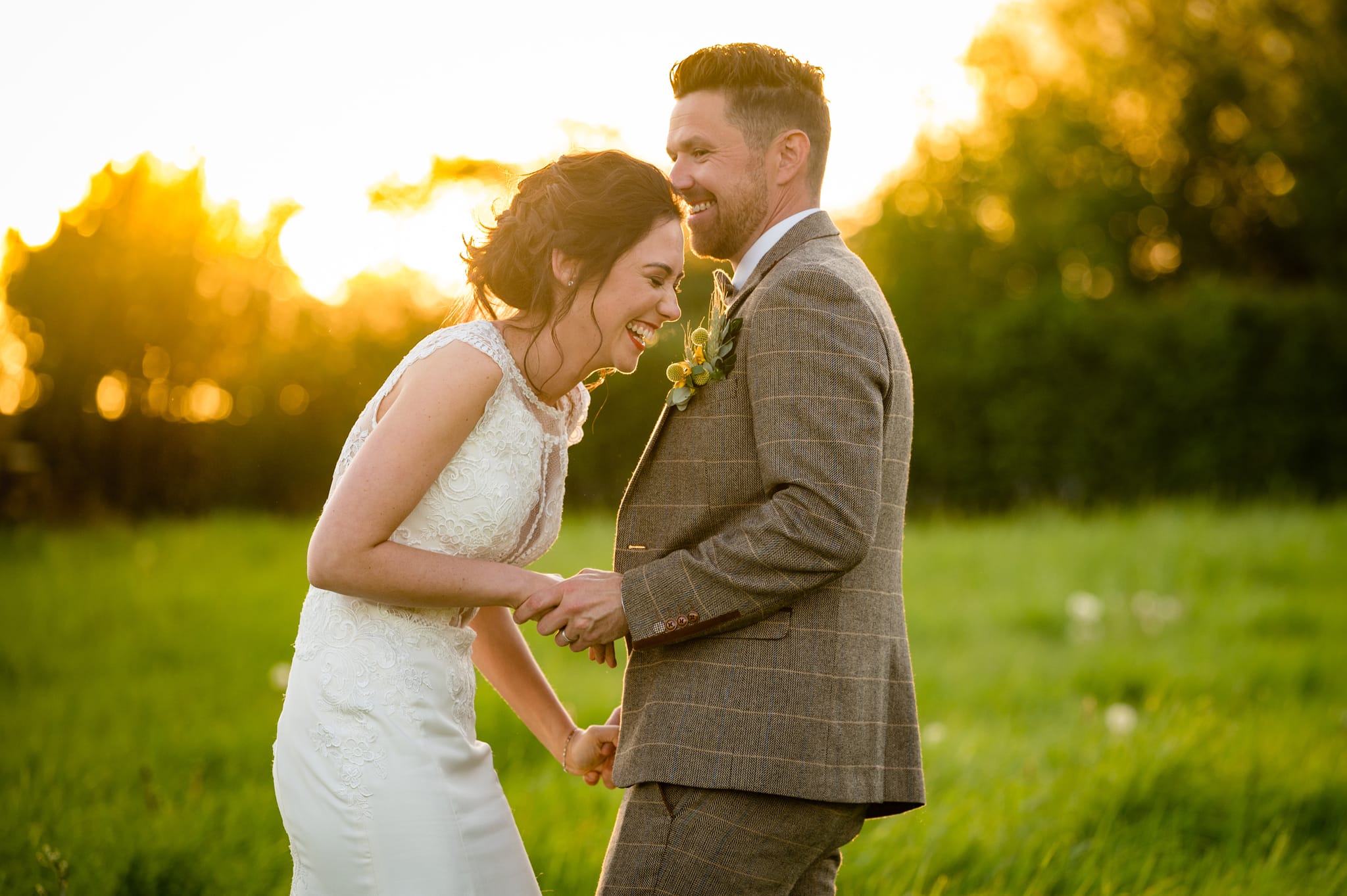 Bride and groom laughing together in a field with golden hour sunlight behind them