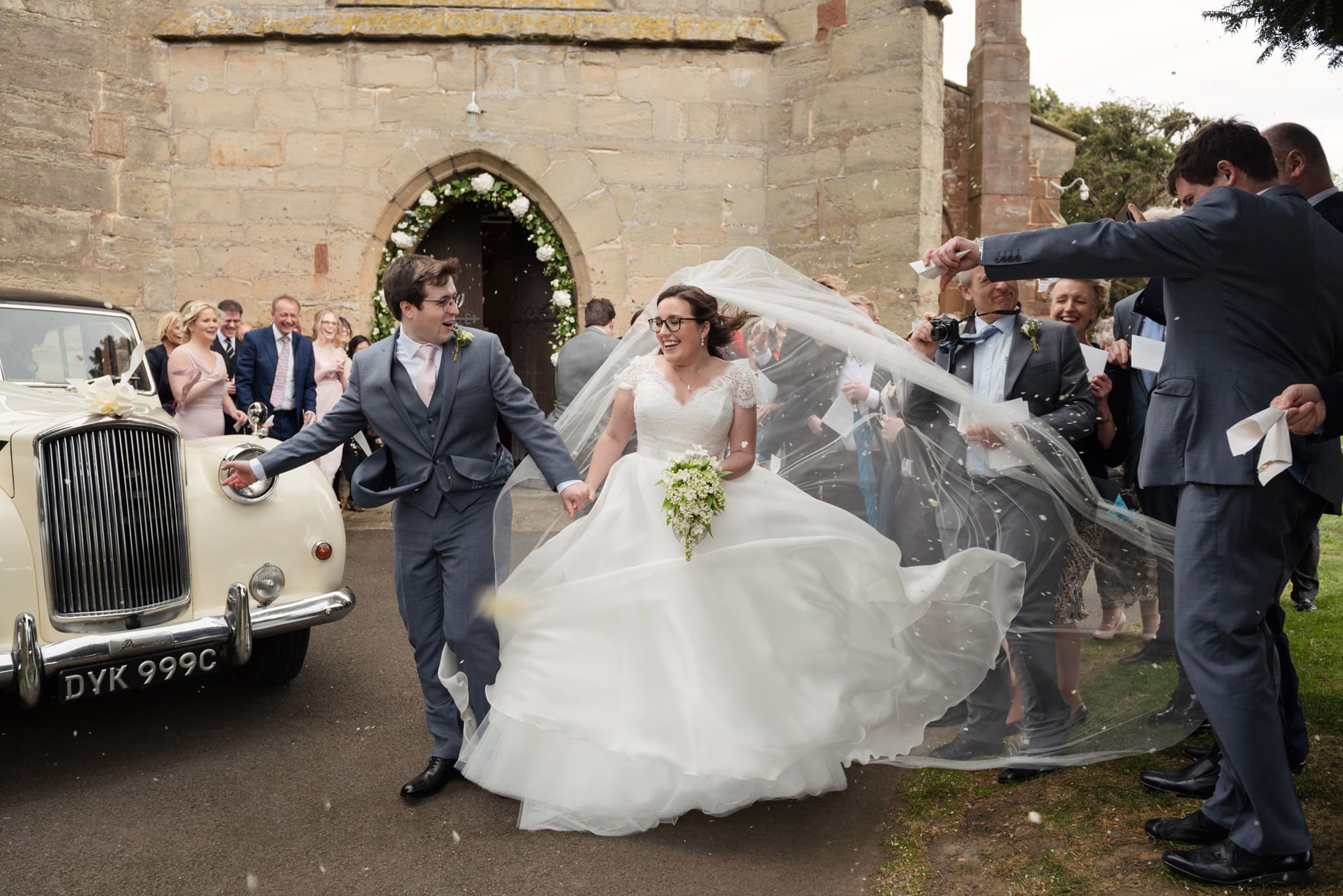 Bride and groom battling the wind as they leave church