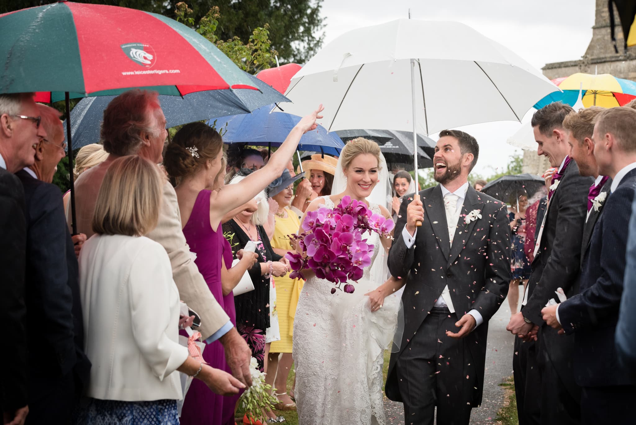 Bride and groom walking confetti line under umbrellas