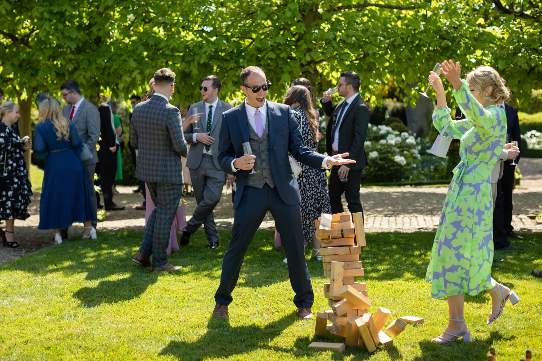 Two wedding guests throwing their arms in the air as the giant jenga tower falls