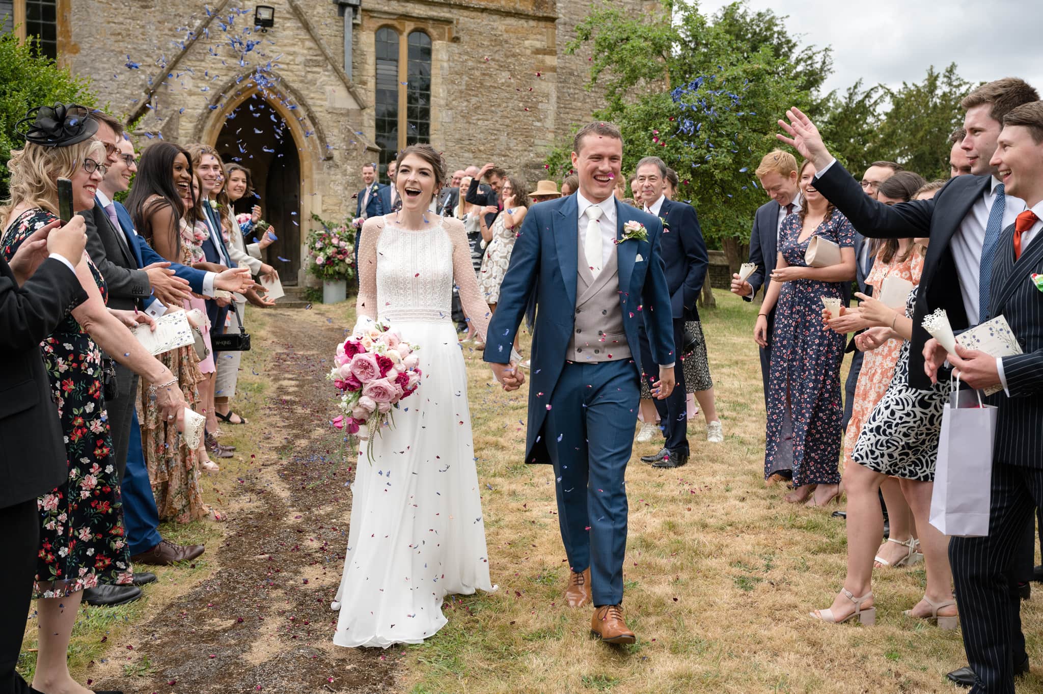 Bride and groom walking through a confetti line at Courteenhall church