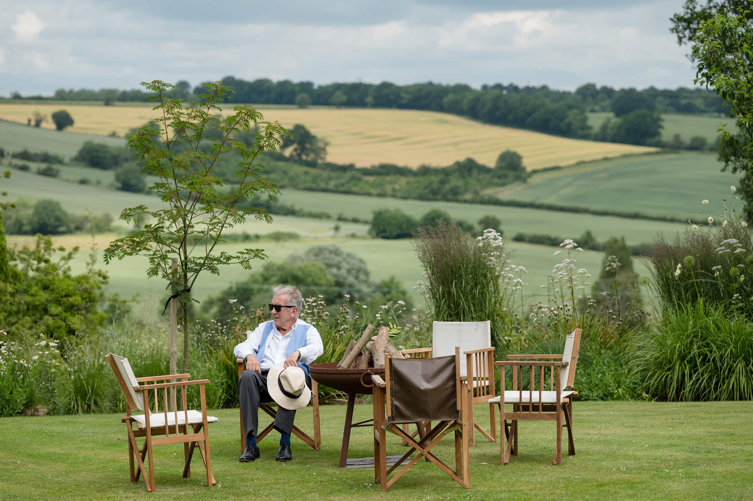 The bride's dad sitting on garden furniture in front of a countryside view