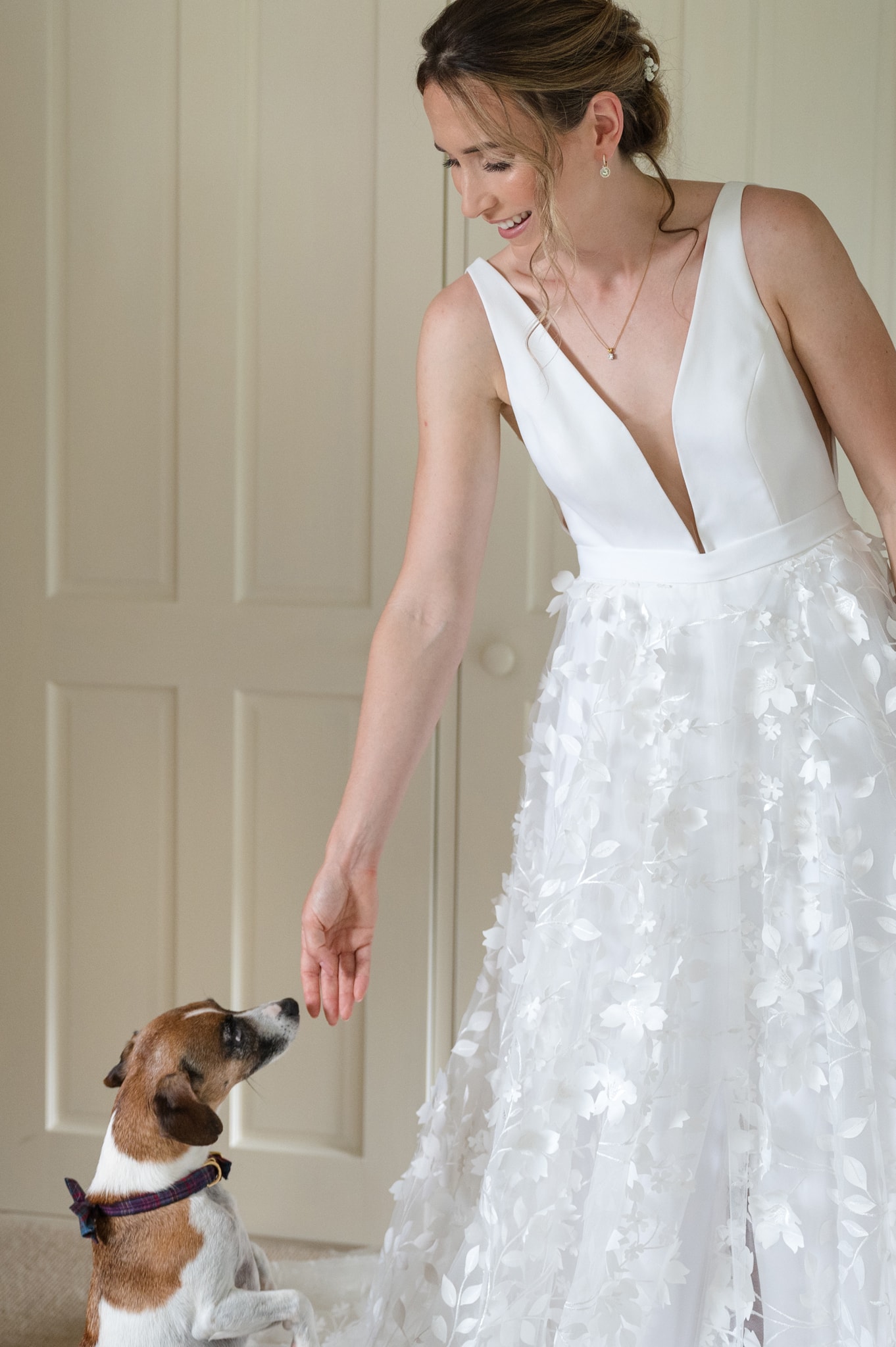 The bride reaching out her hand to stroke her dog who is standing up on its back legs to get to her