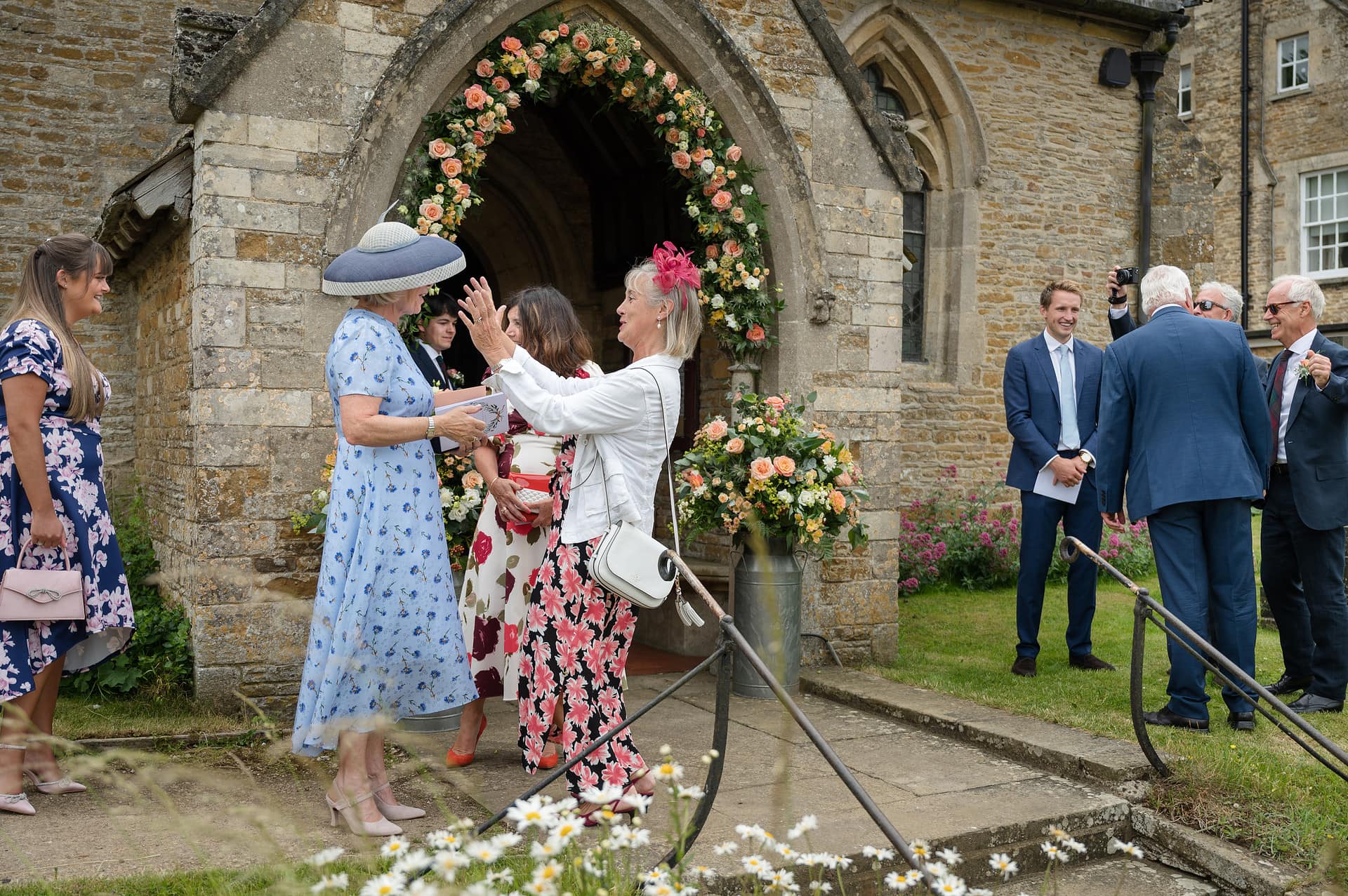 Wedding guests reaching out to hug each other as they arrive at Wing church in Rutland