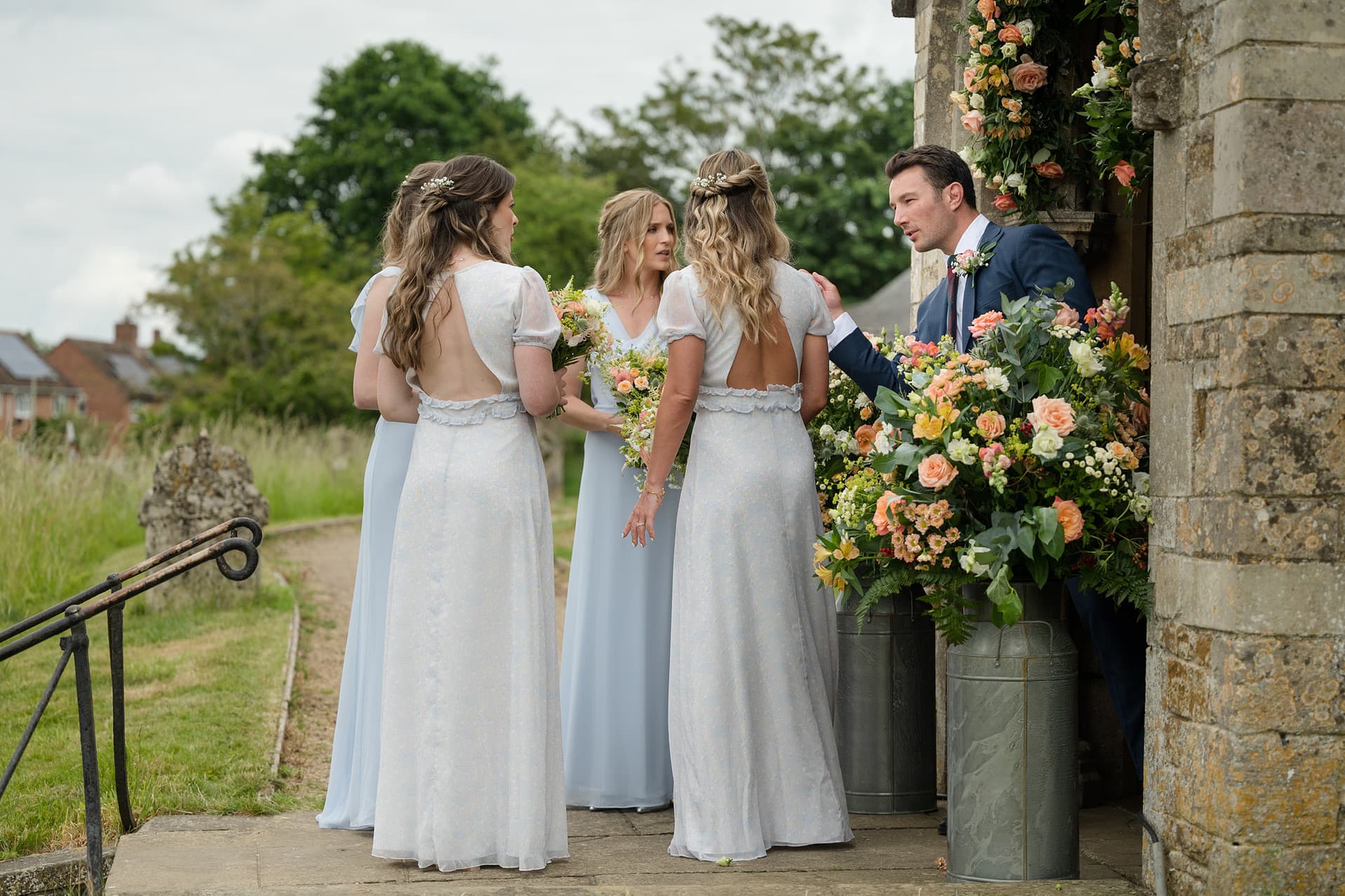 The best man popping his head through the church door to chat to the bridesmaids outside Wing church in Rutland