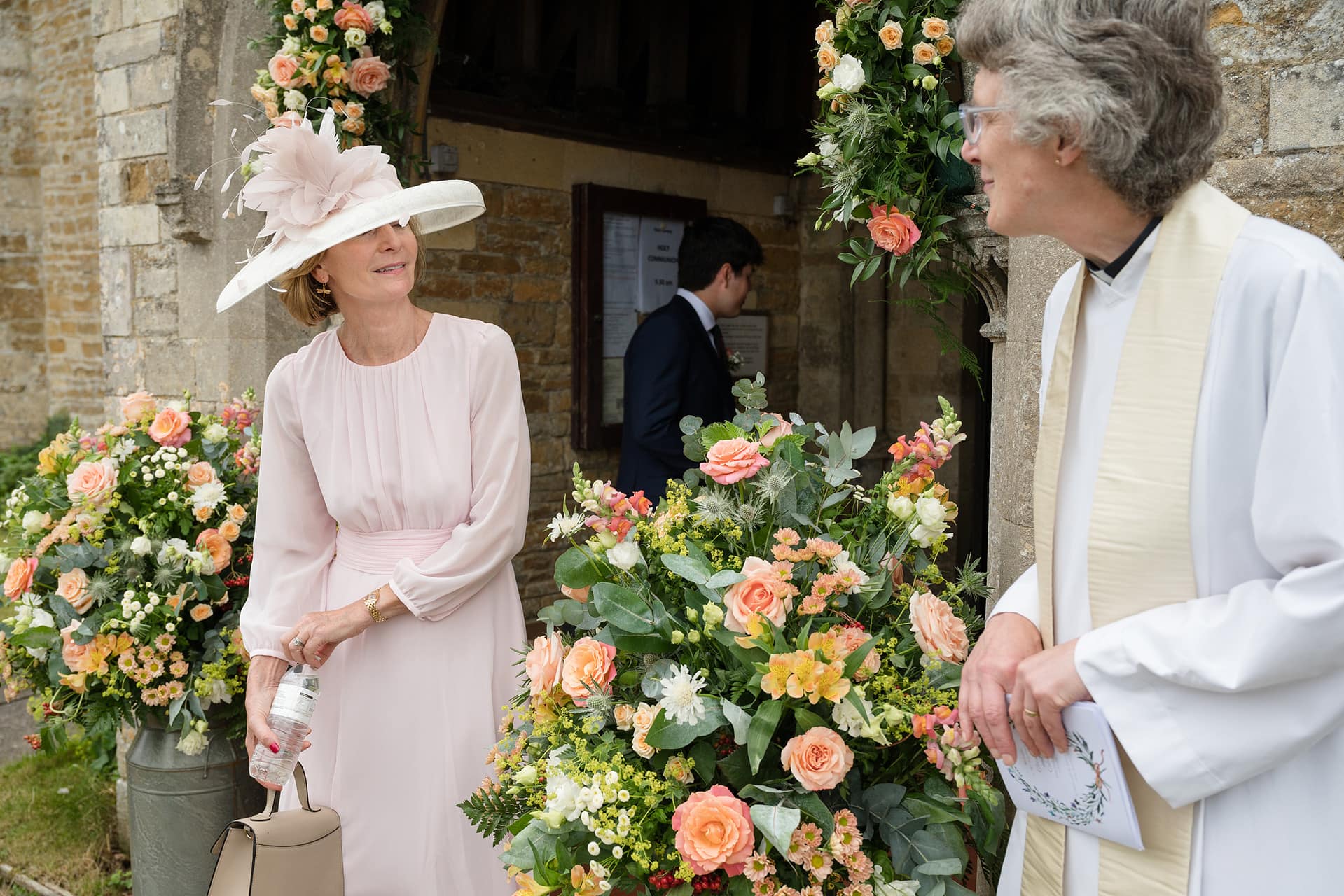 The bride's mum chatting with the vicar as they wait for the bride to arrive outside Wing church in Rutland