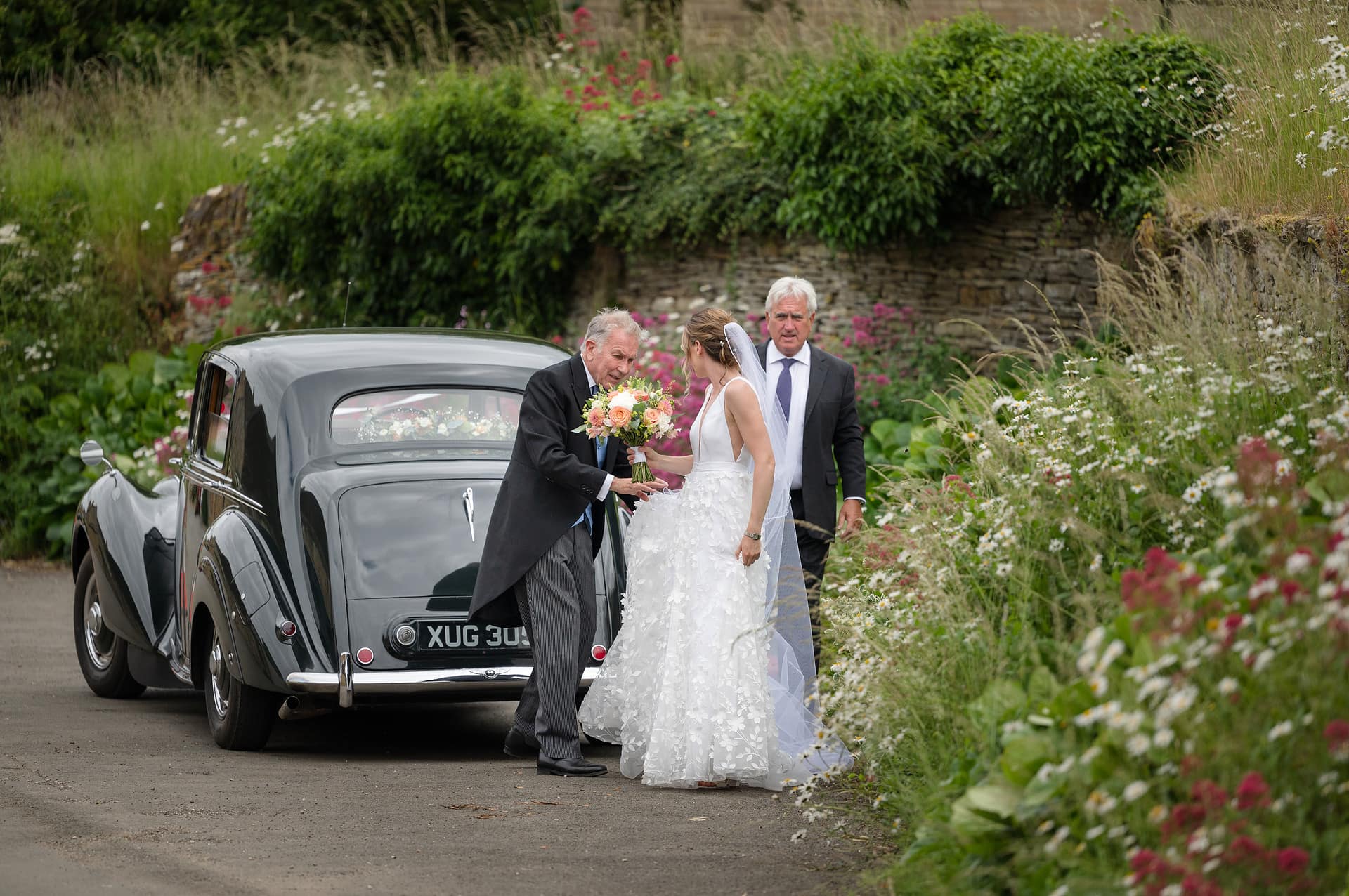 The bride's dad helping the bride with her dress and bouquet after getting out of the wedding car outside Wing church in Rutland