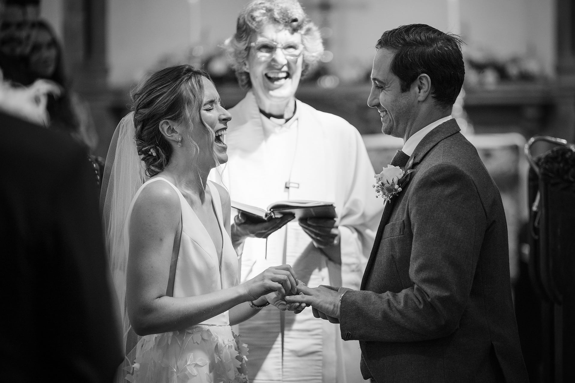 Bride laughing her head off as she tries to put the groom's wedding ring on too soon