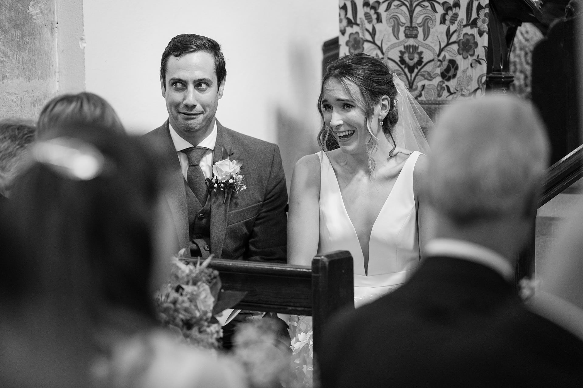 The bride and groom pulling funny faces at the vicar's address in their marriage ceremony at Wing church in Rutland