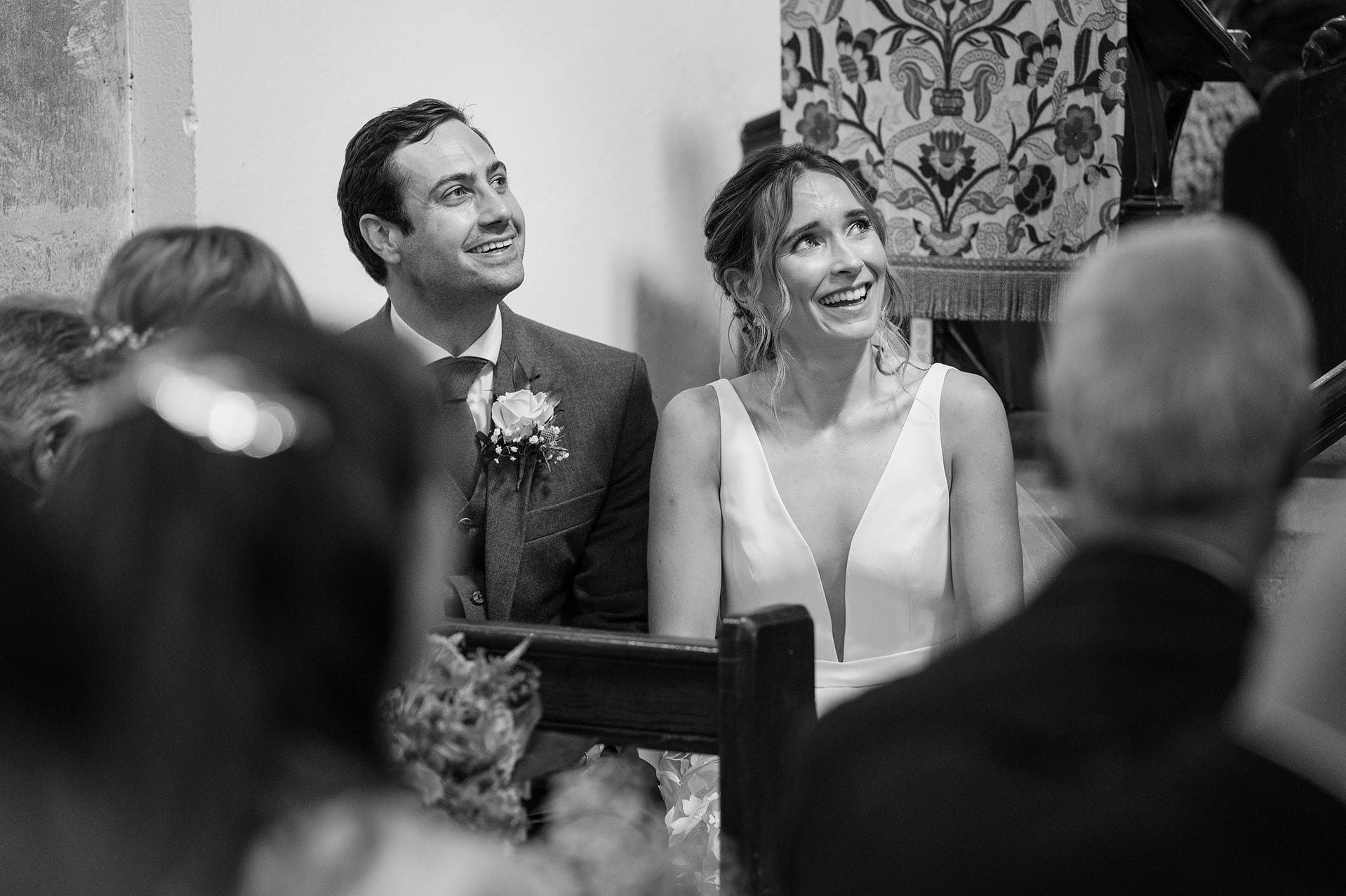 The bride and groom laughing during the vicar's address in their marriage ceremony at Wing church in Rutland