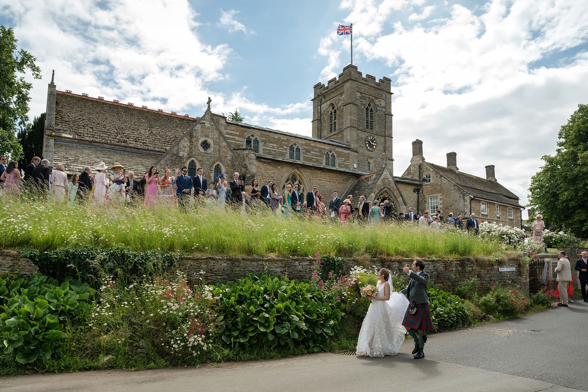 Bride and groom waving at their wedding guests as they leave Wing church in Rutland