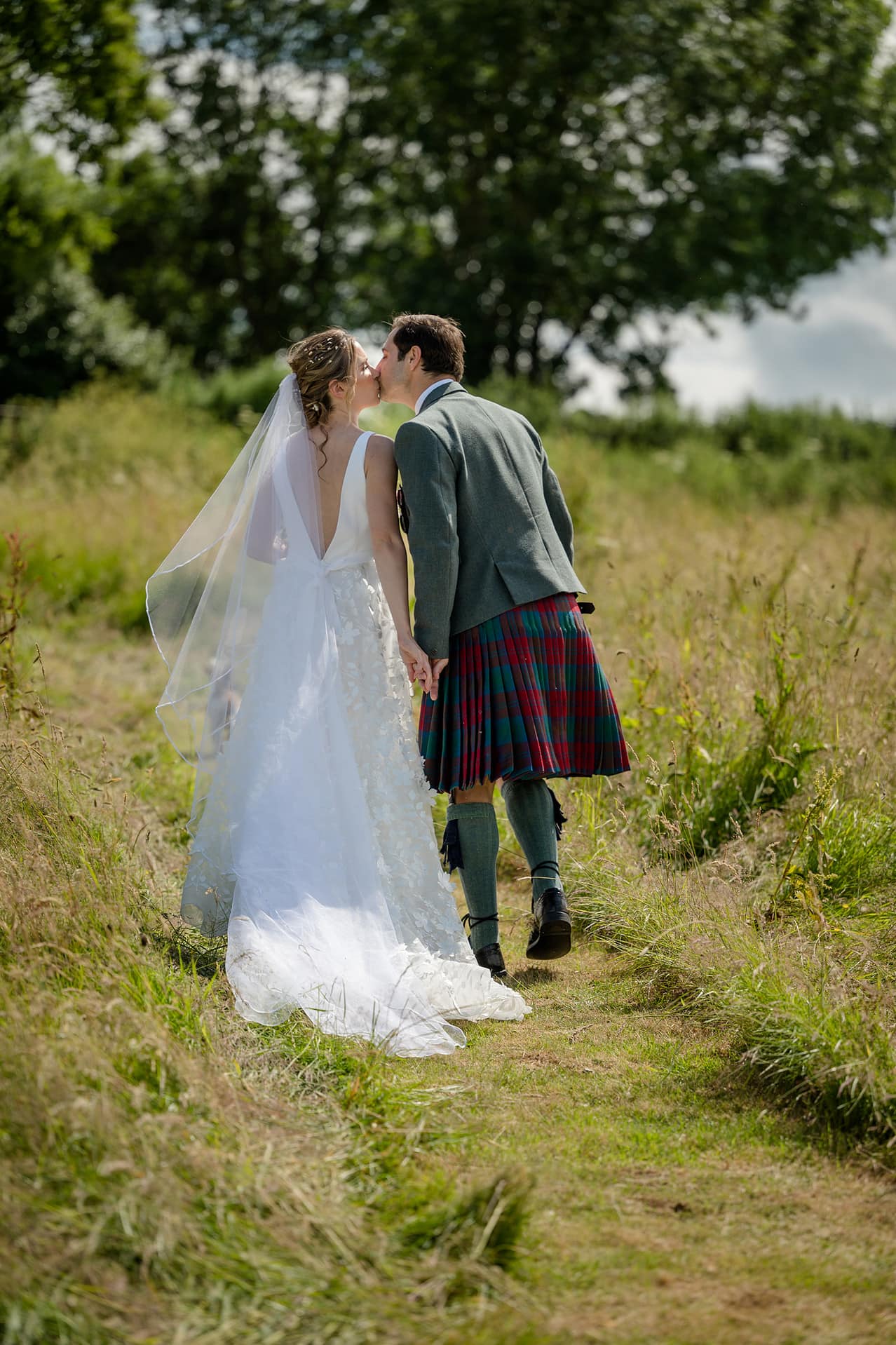 Bride and groom sharing a quick kiss as they walk up a grassy hill