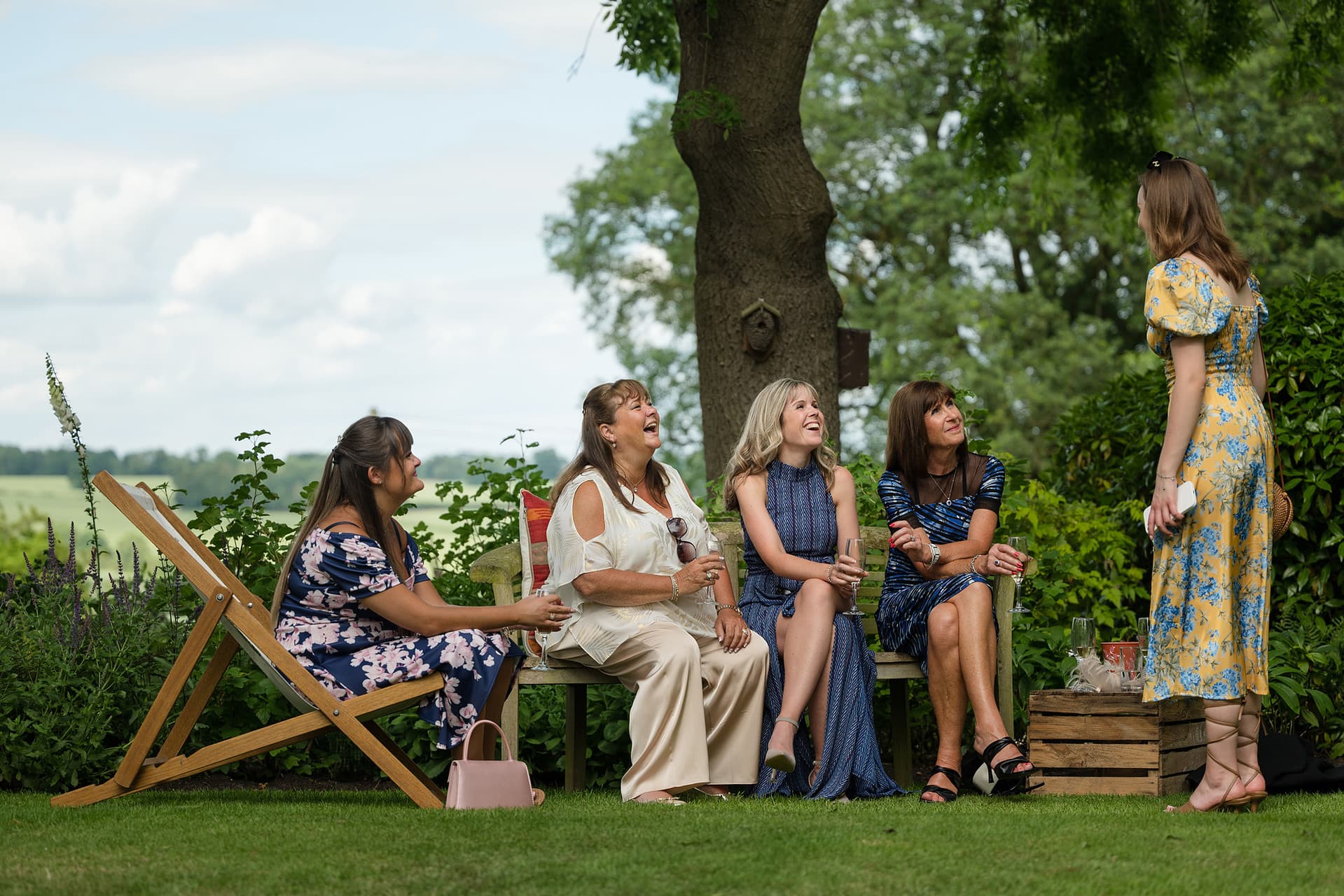 A group of female wedding guests gathered on a bench and deckchairs during the drinks reception