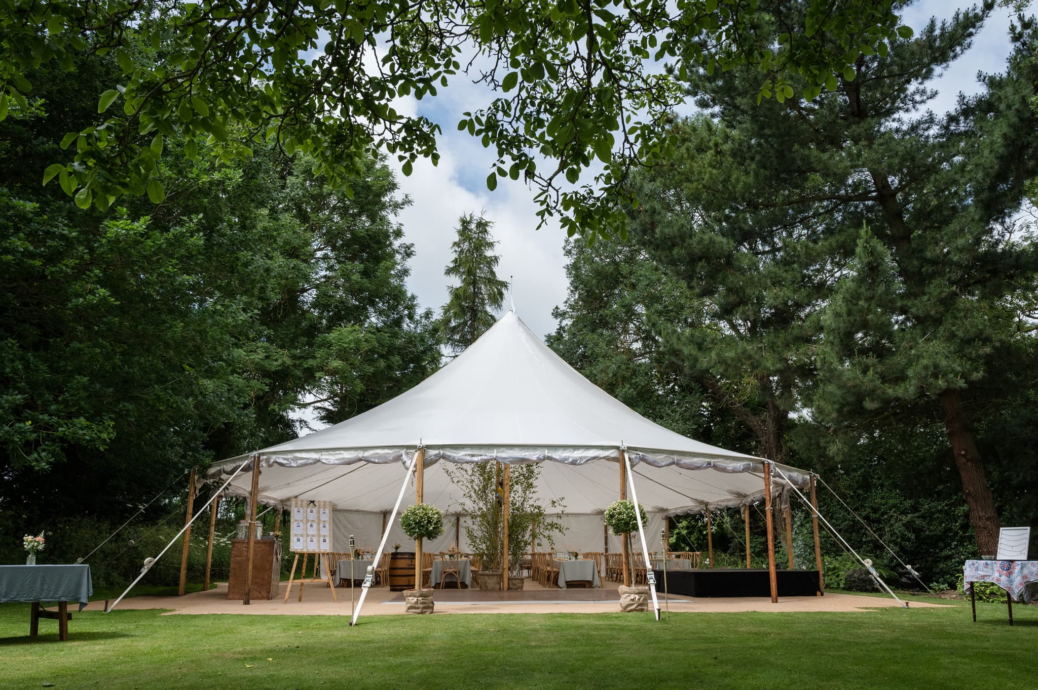 A sailcloth tent marquee with the sides raised nestled amongst trees for a wedding