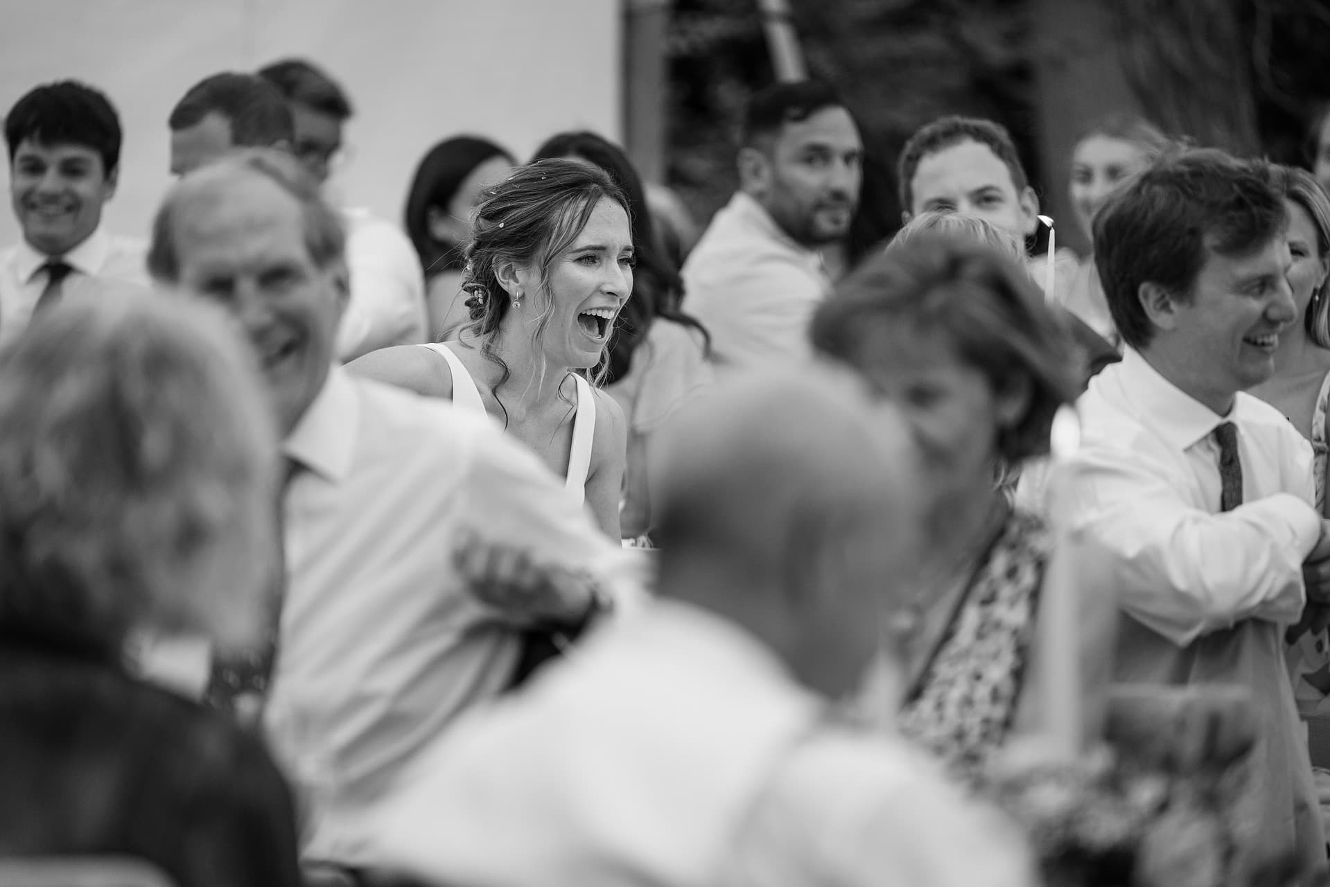 The bride laughing and surrounded by guests during the speeches