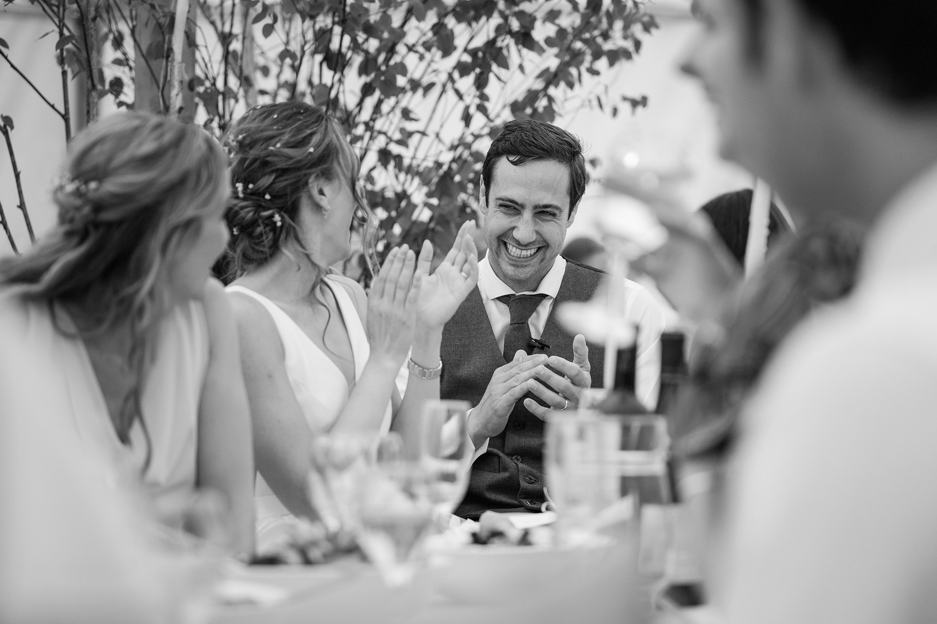 The groom grinning from ear to ear as he laughs at the best man's speech