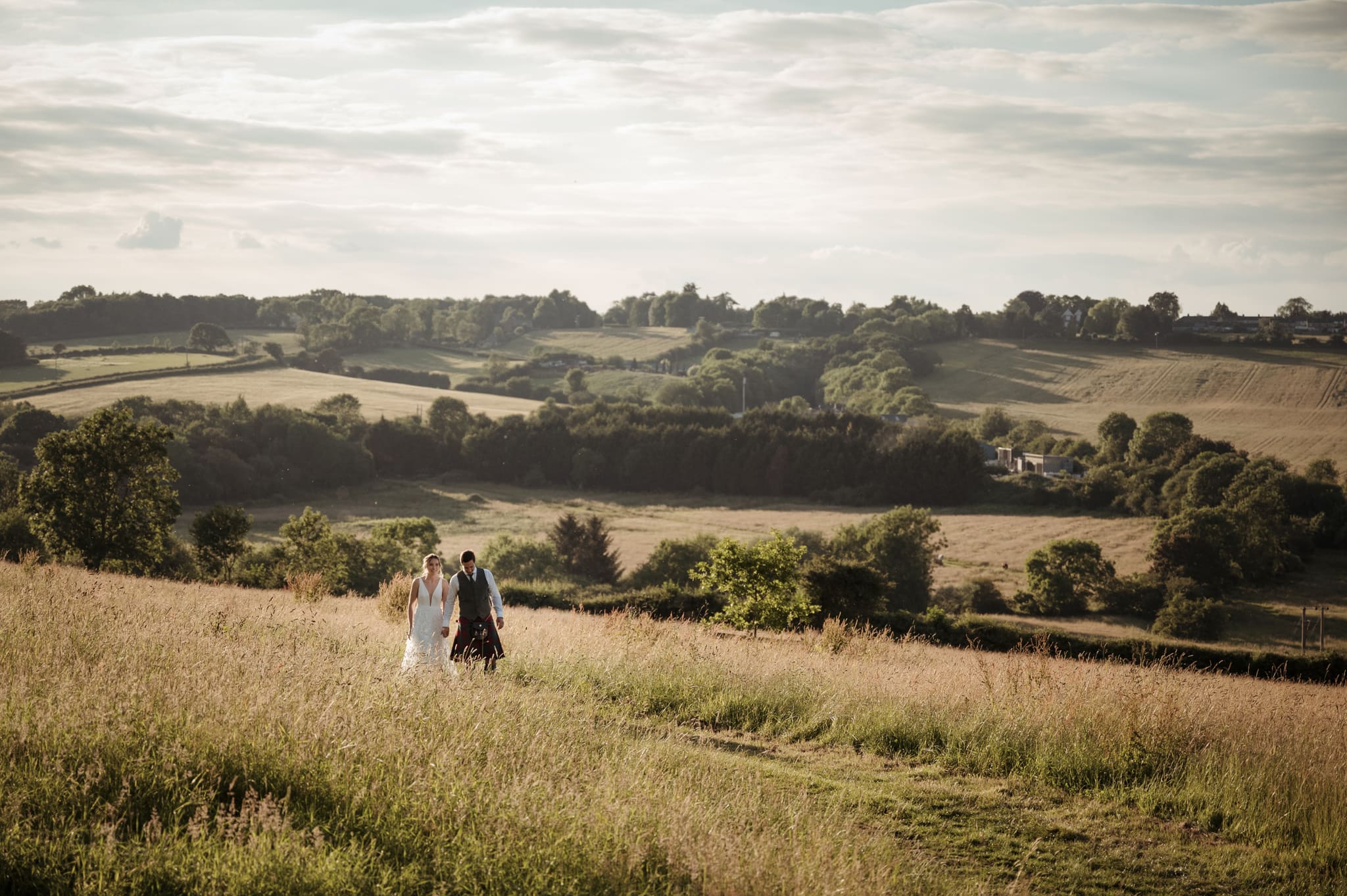 Bride and groom walking through a field during golden hour