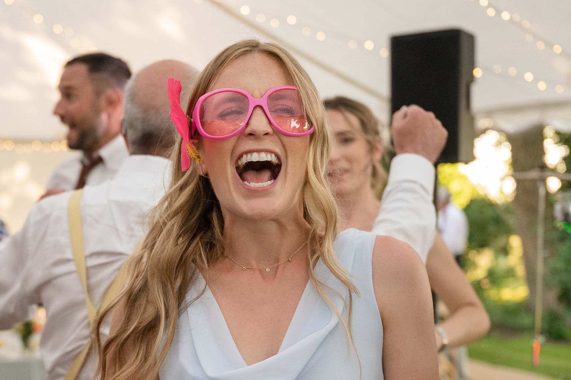 A wedding guest wearing bright pink dress-up sunglasses on the dancefloor