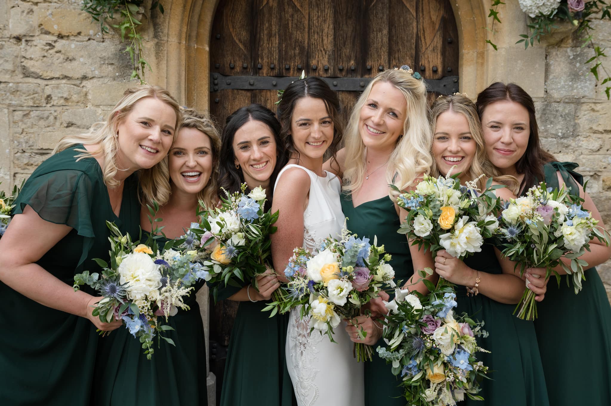 The bride and her bridesmaids posing for a group photo outside the front door of Notley Abbey