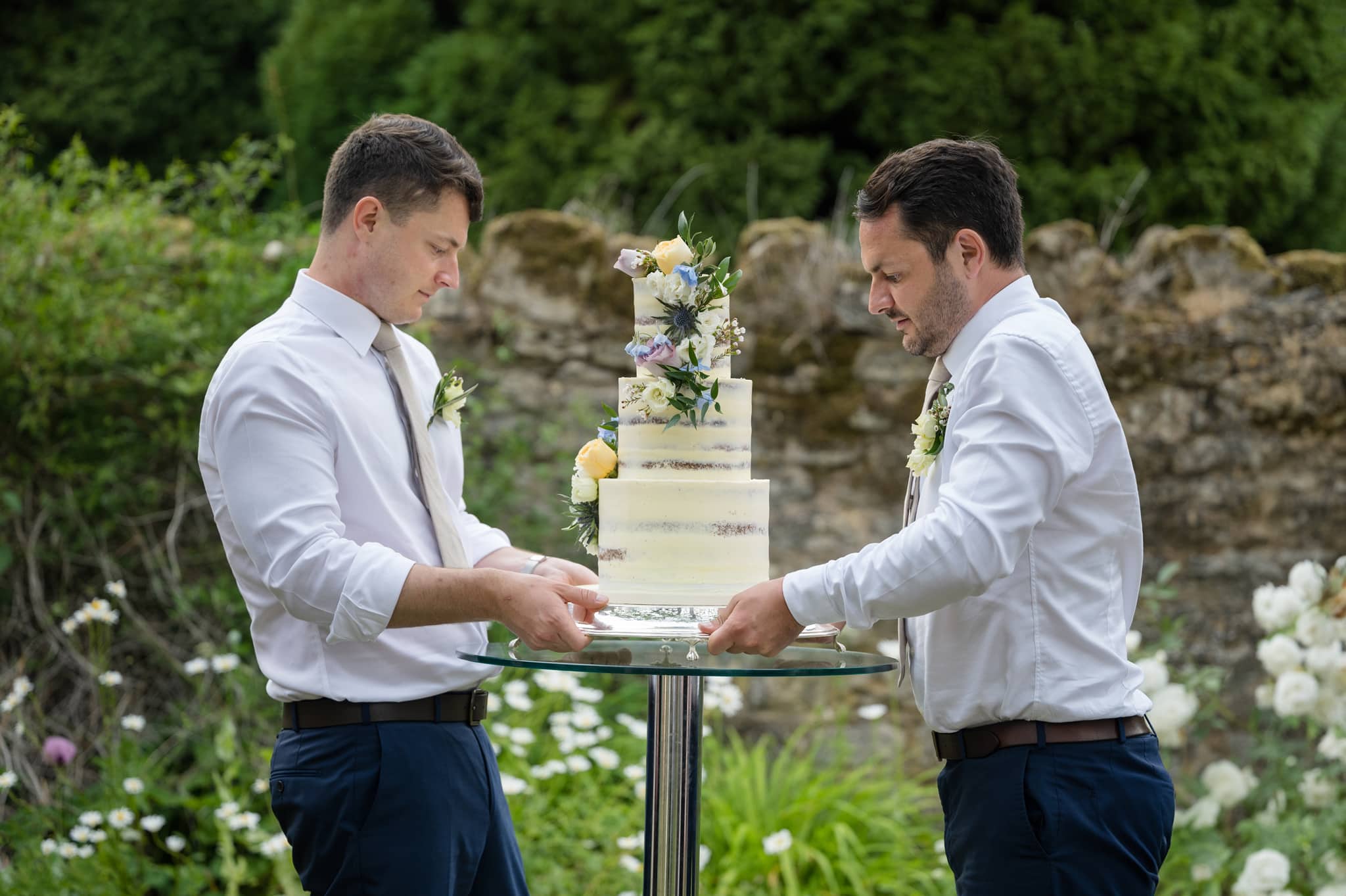 Two ushers placing the wedding cake on a table outside at Notley Abbey